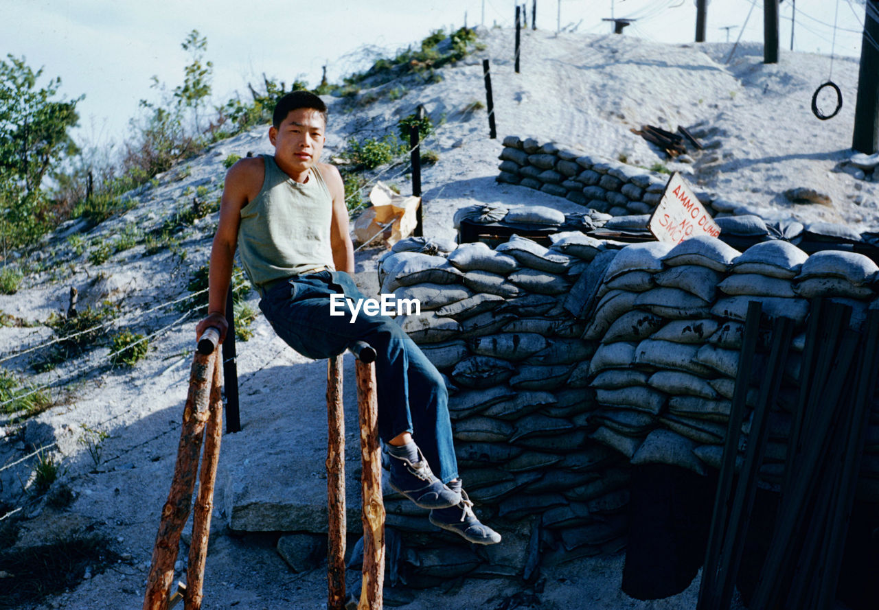 FULL LENGTH PORTRAIT OF YOUNG MAN SITTING ON WALL