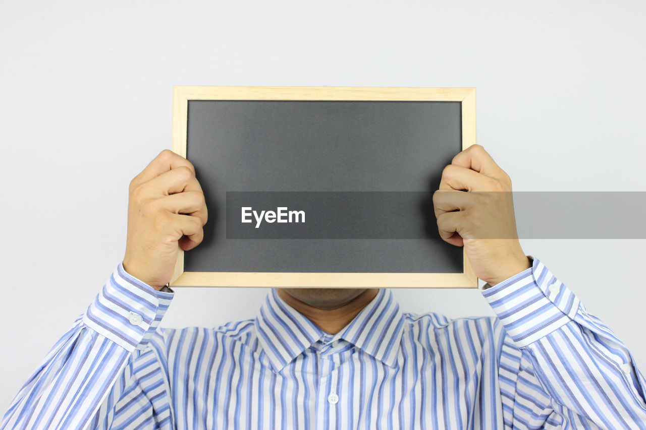 Close-up of man holding blank blackboard against white background