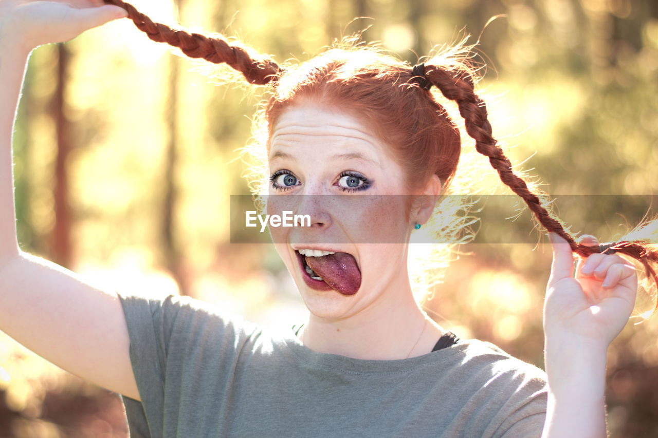 Portrait of woman holding braided hair while sticking out tongue