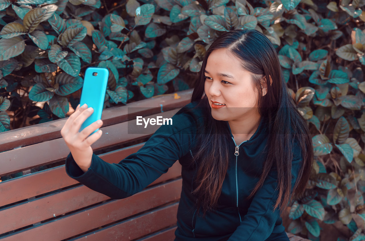 Young woman taking selfie on bench by plants