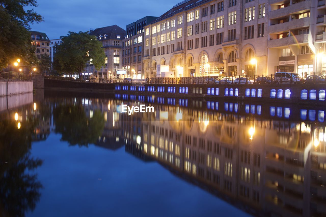 ILLUMINATED BUILDINGS BY LAKE IN CITY AT NIGHT