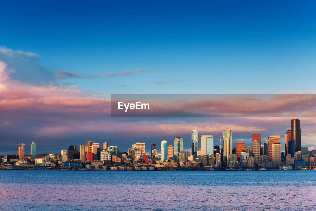 SCENIC VIEW OF SEA BY BUILDINGS AGAINST SKY DURING SUNSET