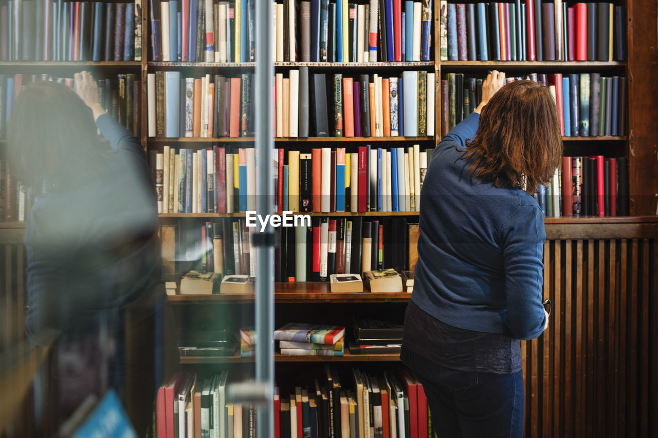 Rear view of librarian arranging books on shelf in antique shop