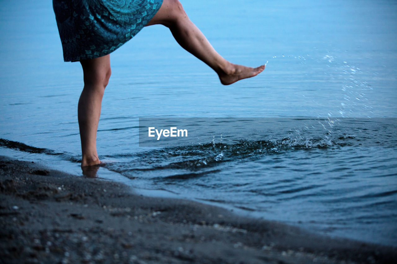 Low section of woman splashing water in sea at beach