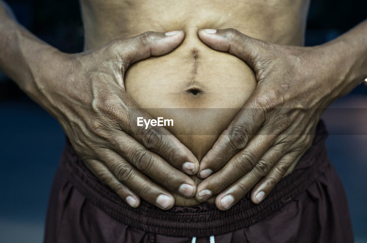 Midsection of man making heart shape on belly