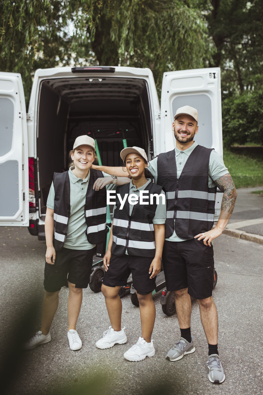 Portrait of smiling male and female coworkers standing against delivery van