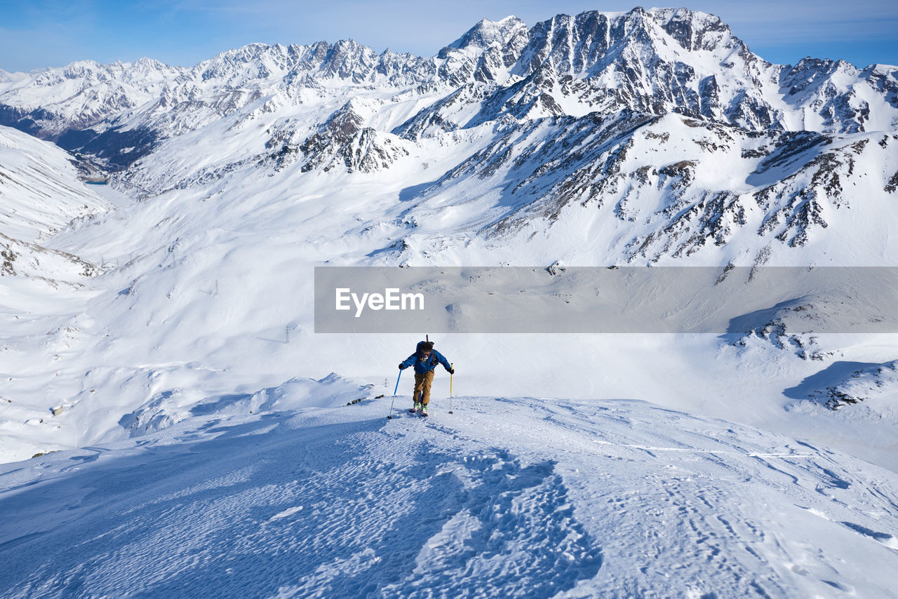 Man ski touring up slow with mountain behind him