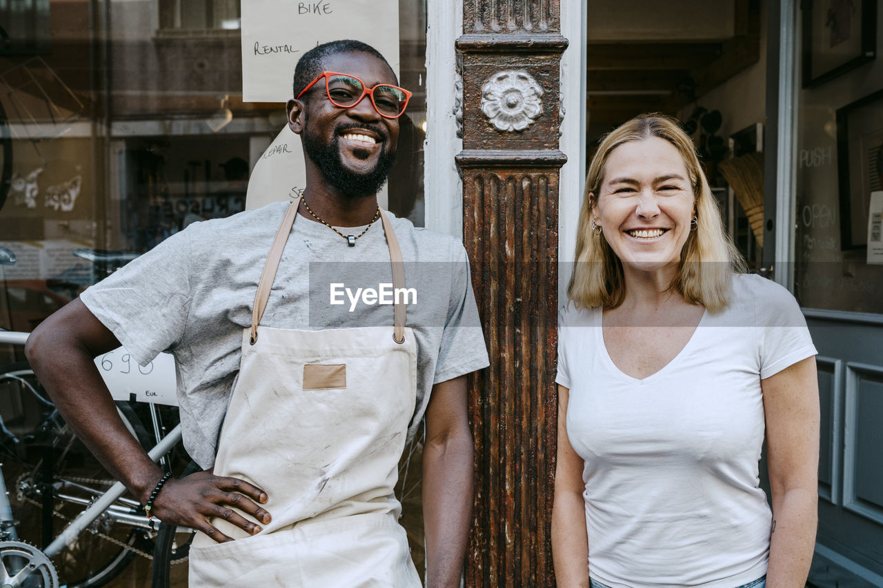 Portrait of cheerful owners standing against bicycle shop