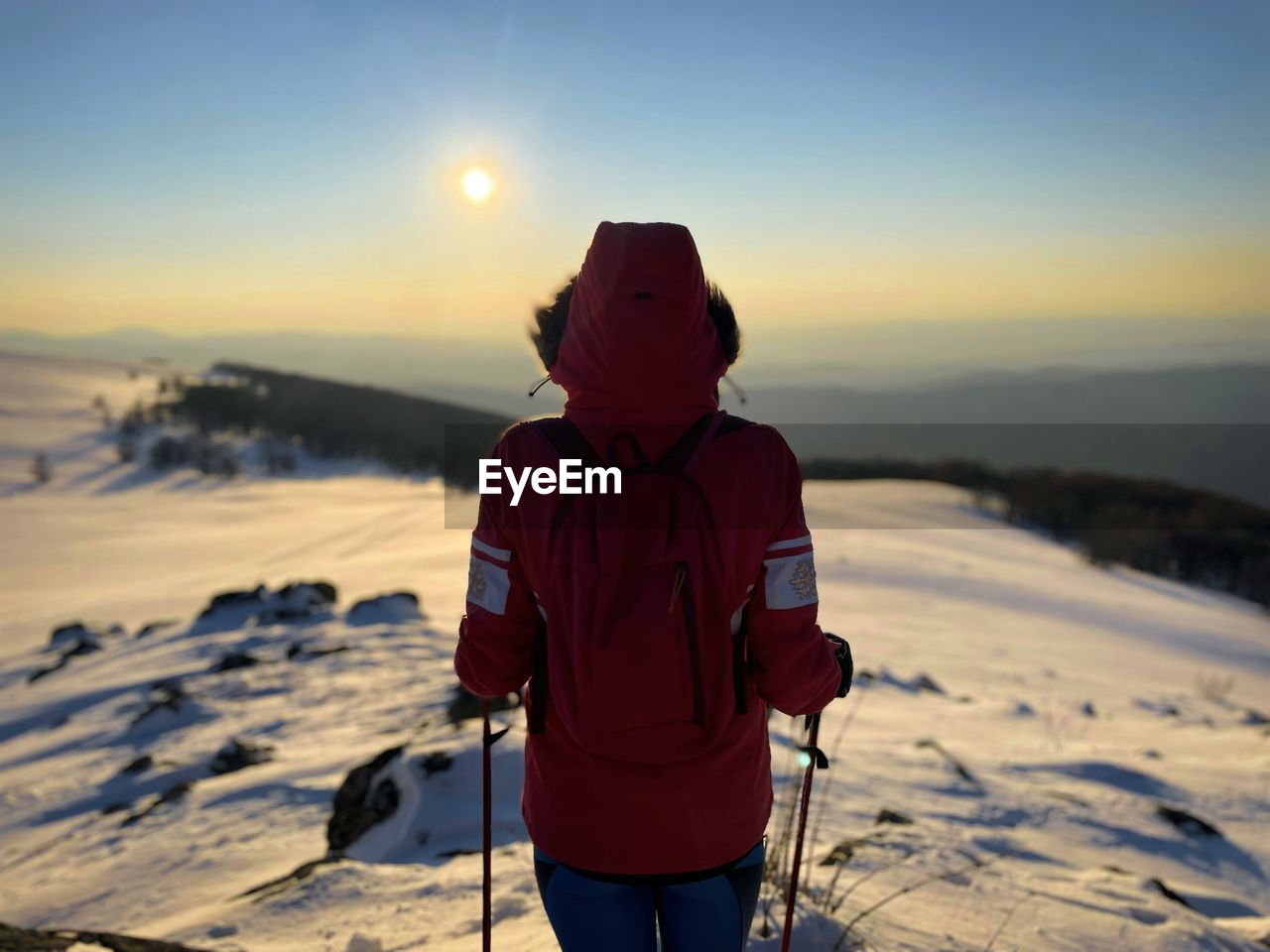 Rear view of woman with hooded winter coat and backpack hiking in the mountains at sunset