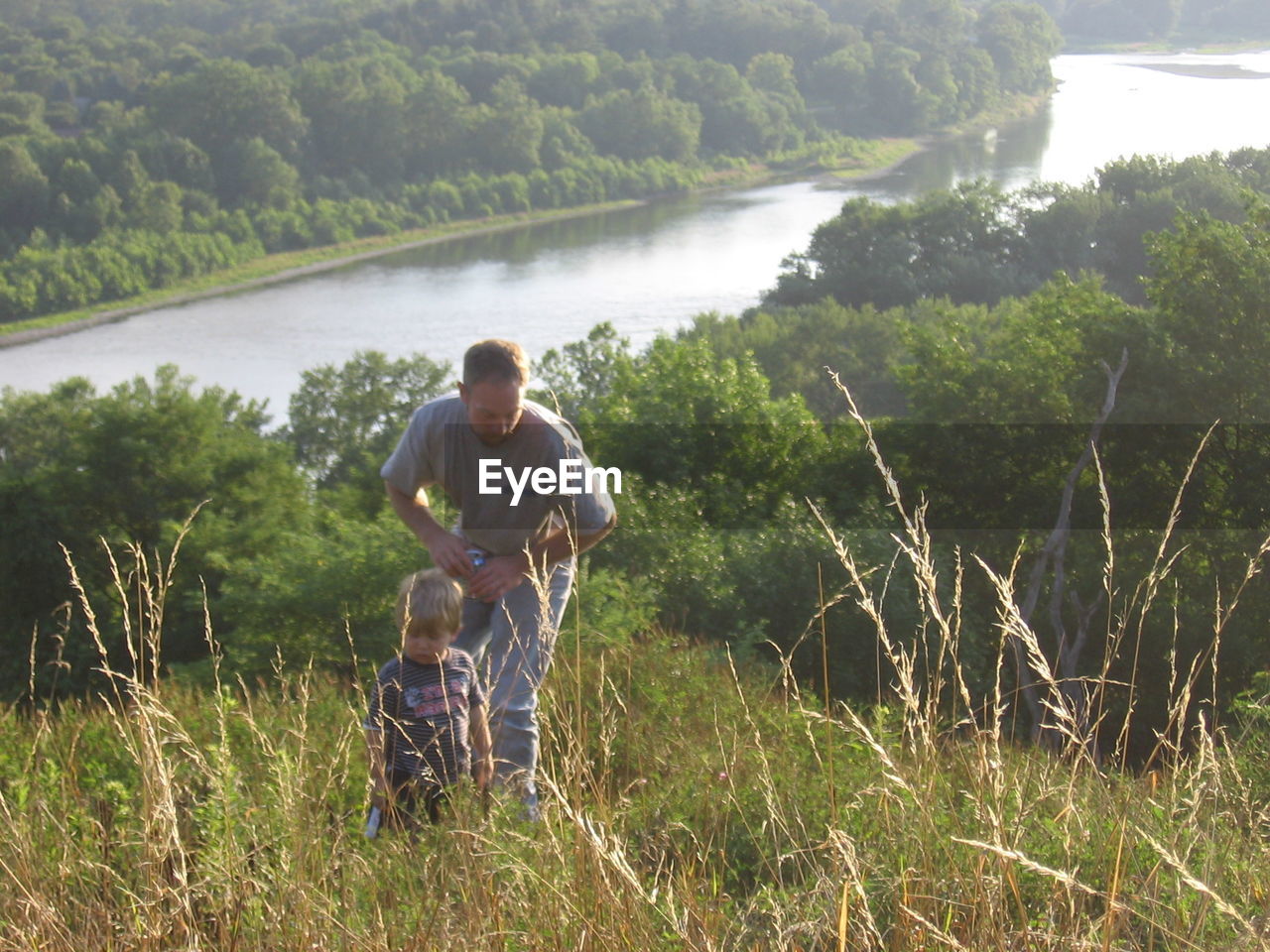 Father with son standing on grassy hill by lake