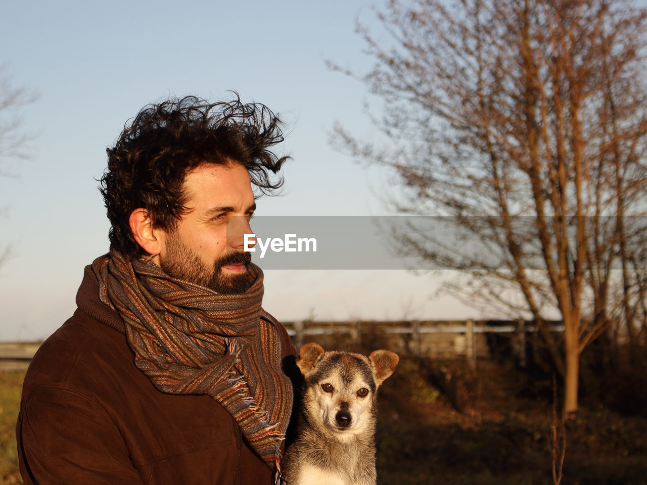 Thoughtful man standing with dog against clear sky during sunset