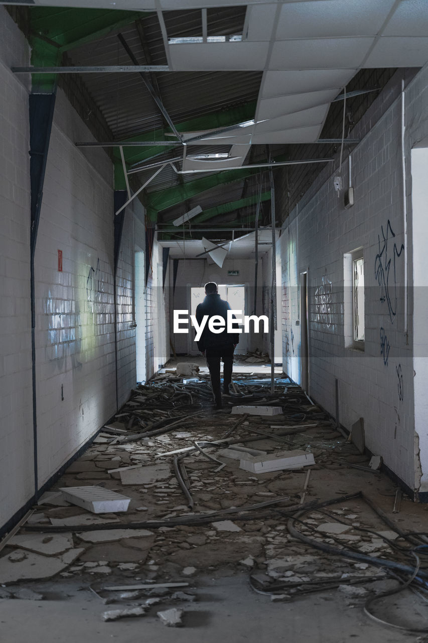 REAR VIEW OF MAN STANDING IN ABANDONED BUILDING