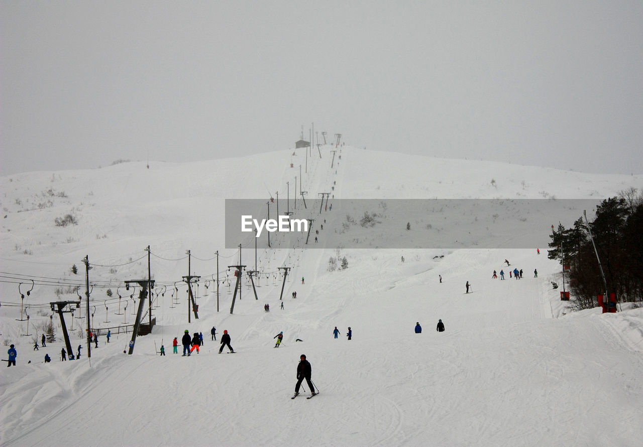 People skiing on snow covered hill against clear sky