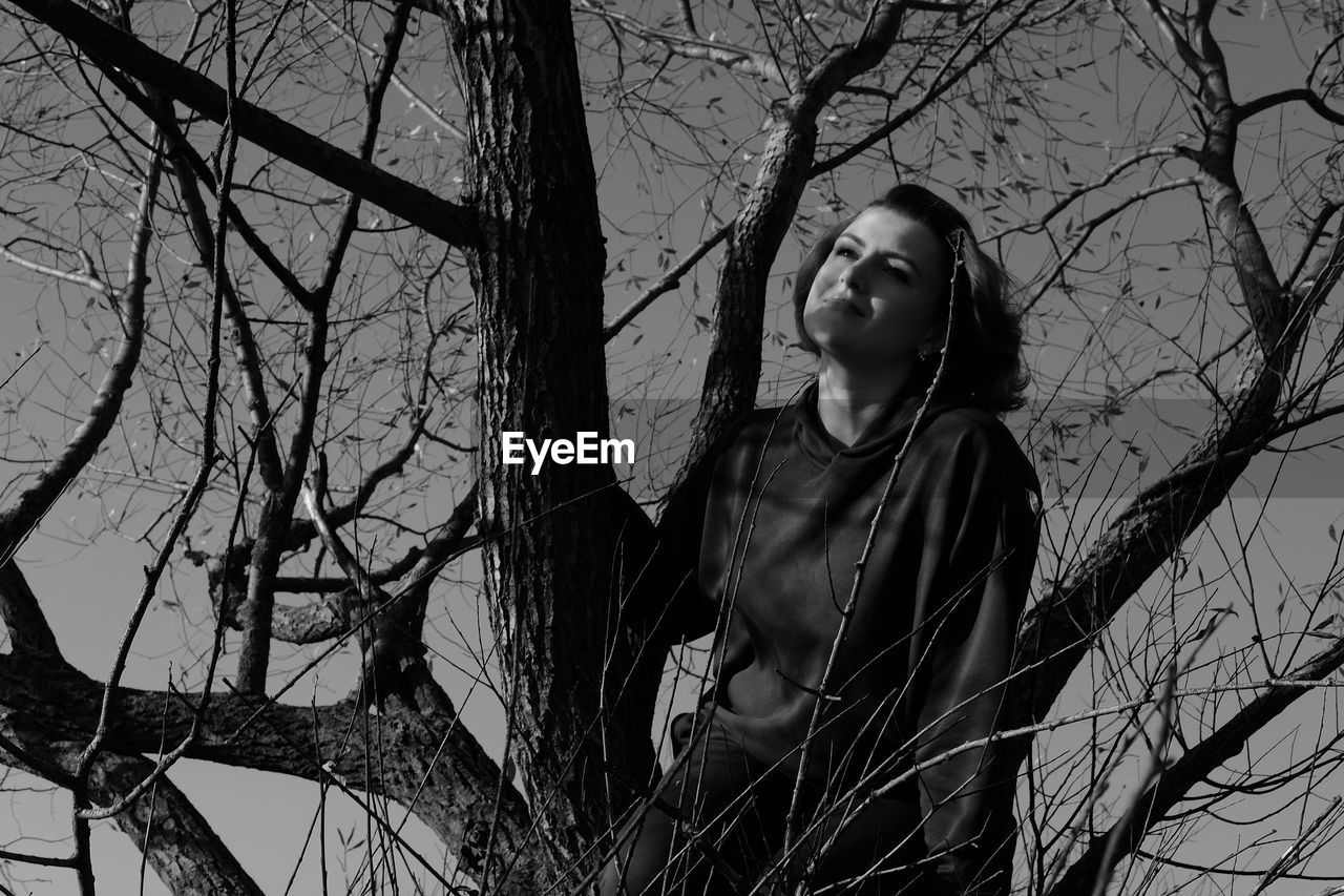 Thoughtful woman looking away while sitting on tree