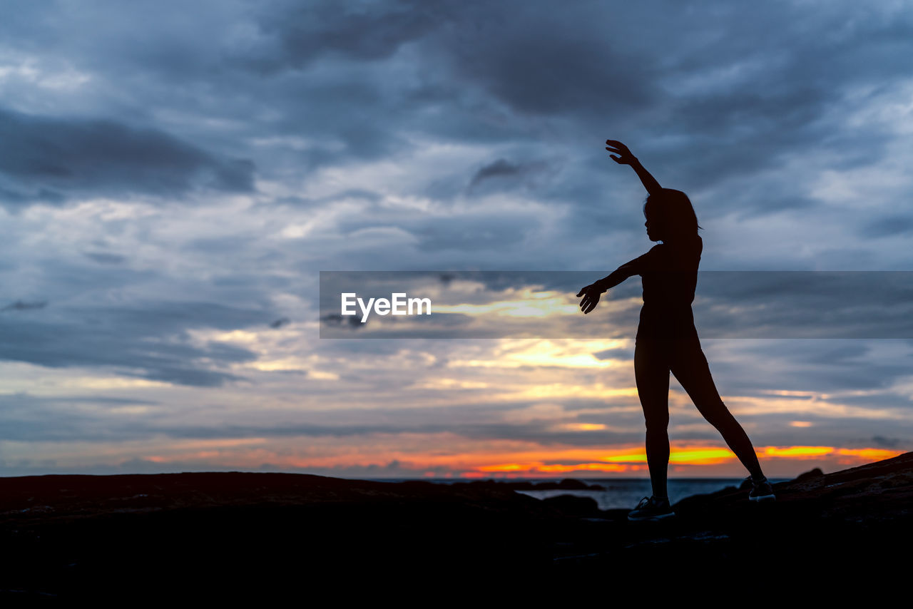 Silhouette woman dancing on land against sky during sunset