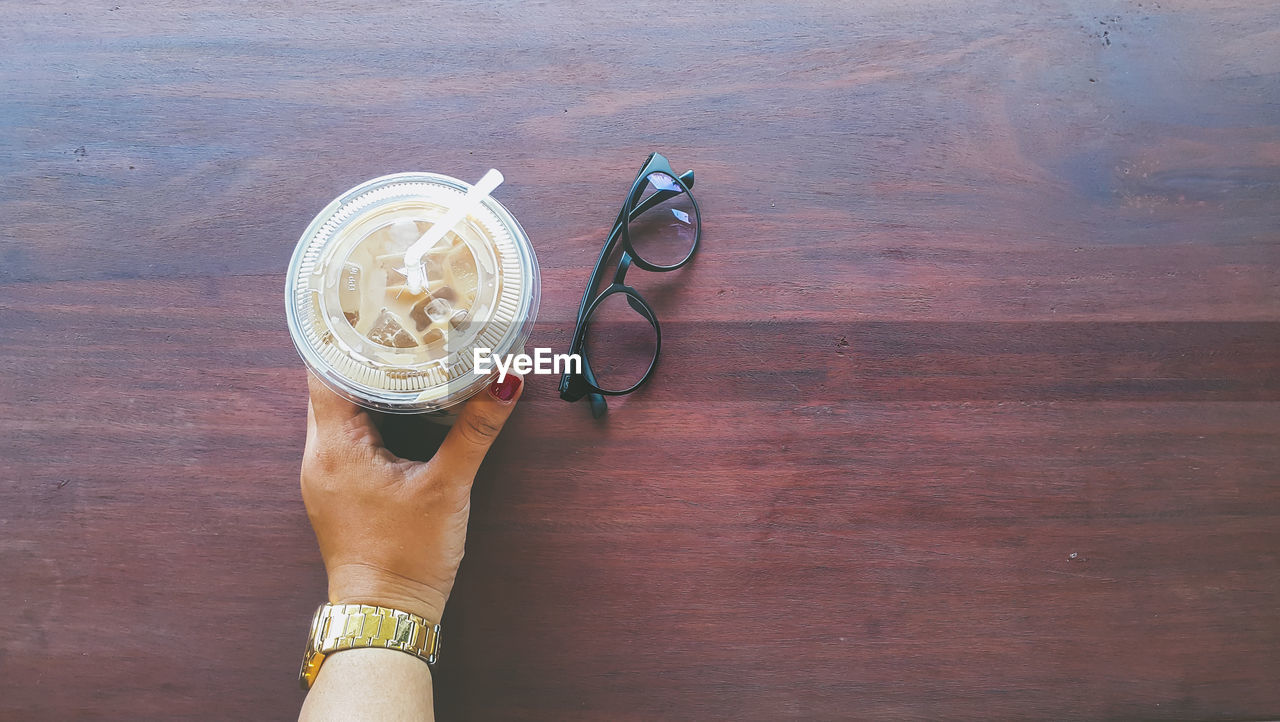 Cropped image of woman holding coffee cup by eyeglasses on table