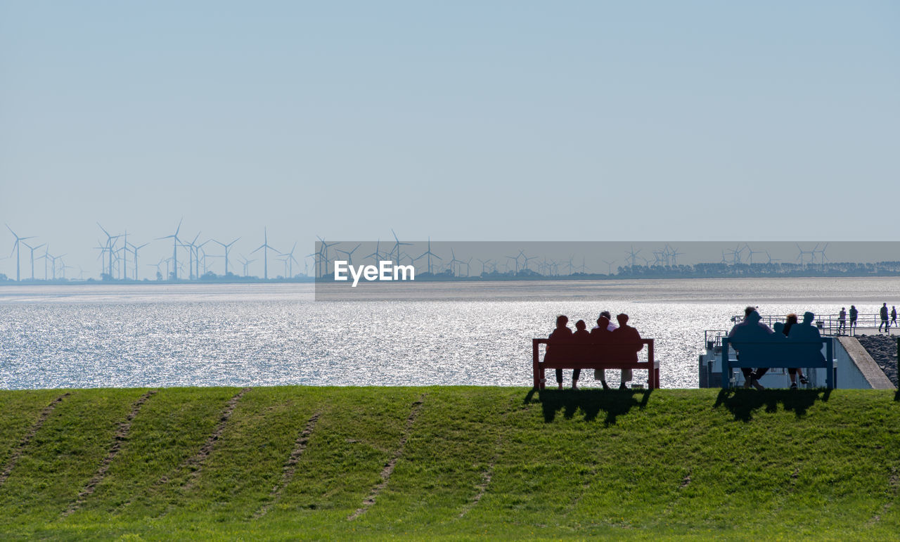 People by beach against clear sky