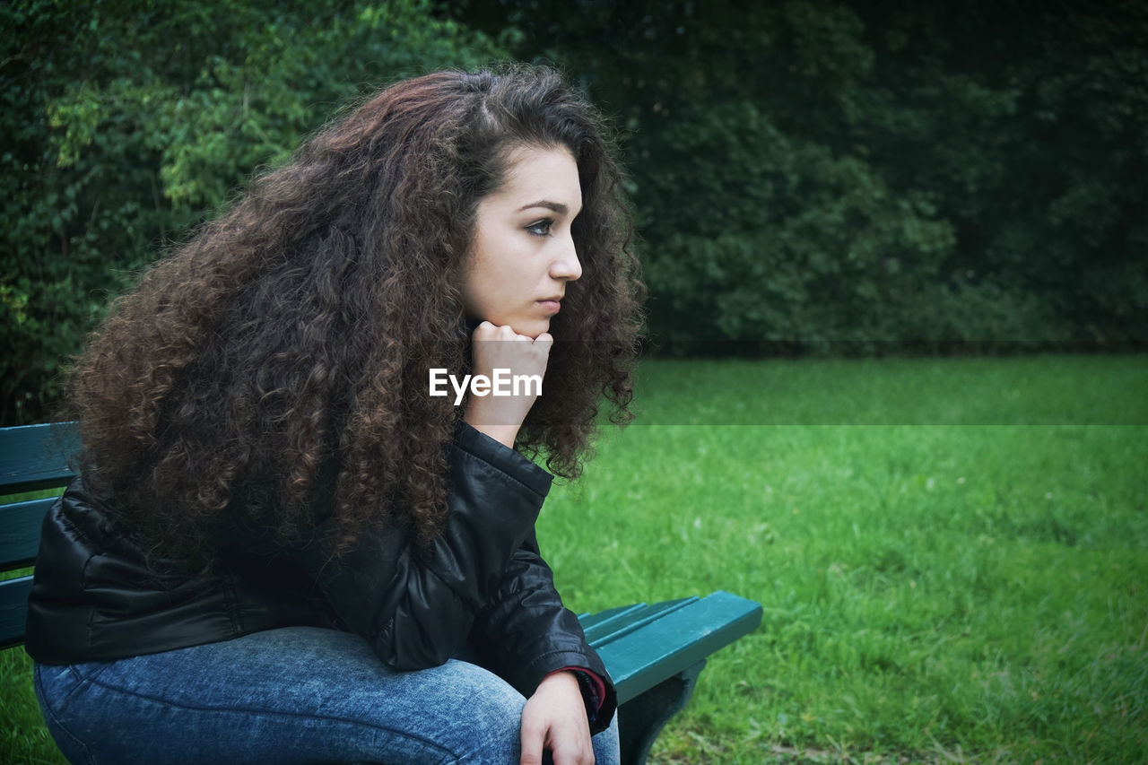 Thoughtful young woman sitting on park bench