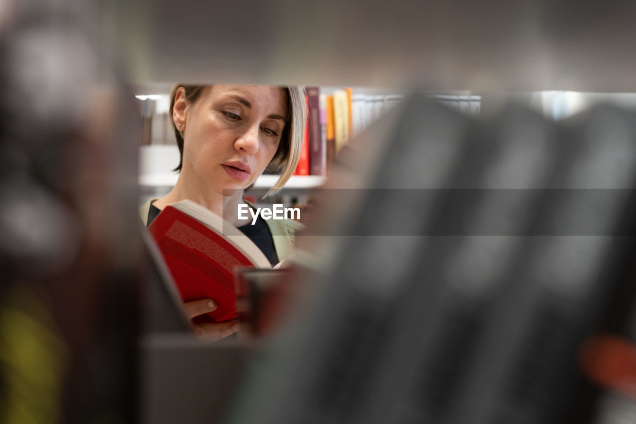 Scandinavian middle-aged woman choosing textbook, looking for literature while preparing for exam