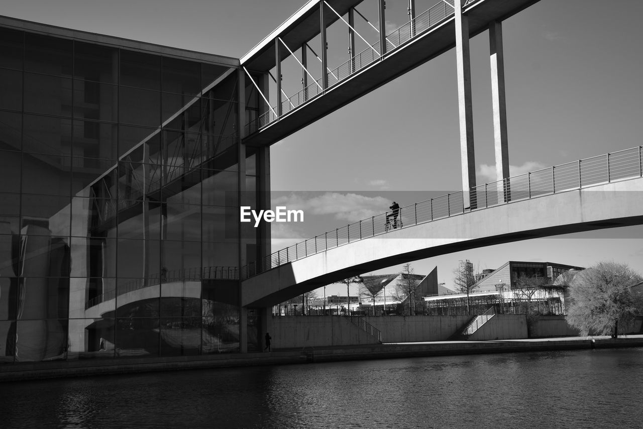 Bridge over river by buildings against sky