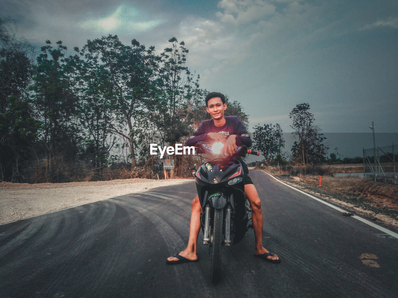 Portrait of man riding motorcycle on road against sky