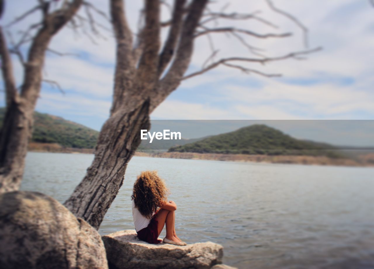 Side view full length of woman sitting on rock against lake