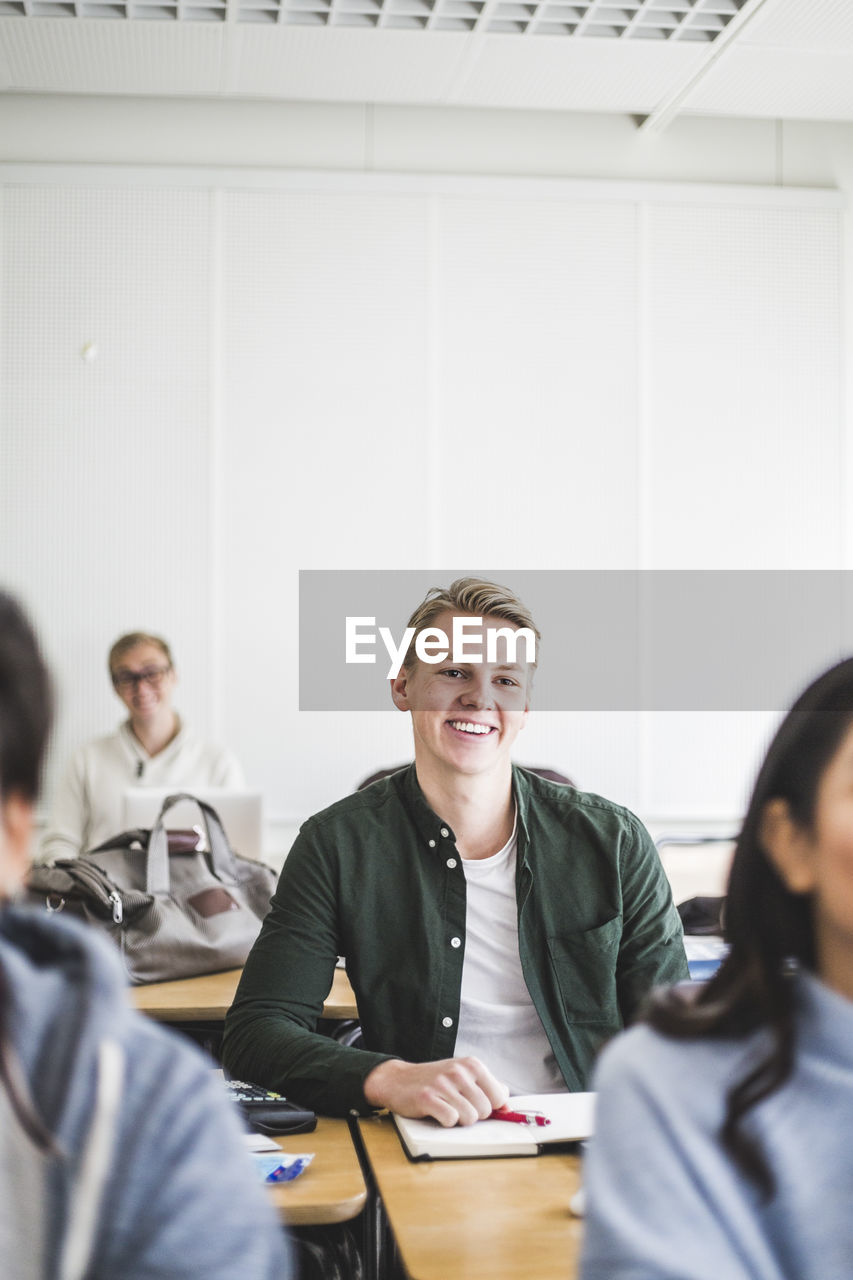 Smiling young man sitting at desk in classroom