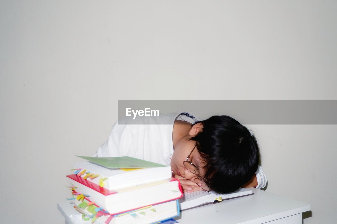 Tired young woman sleeping on books at table against white background