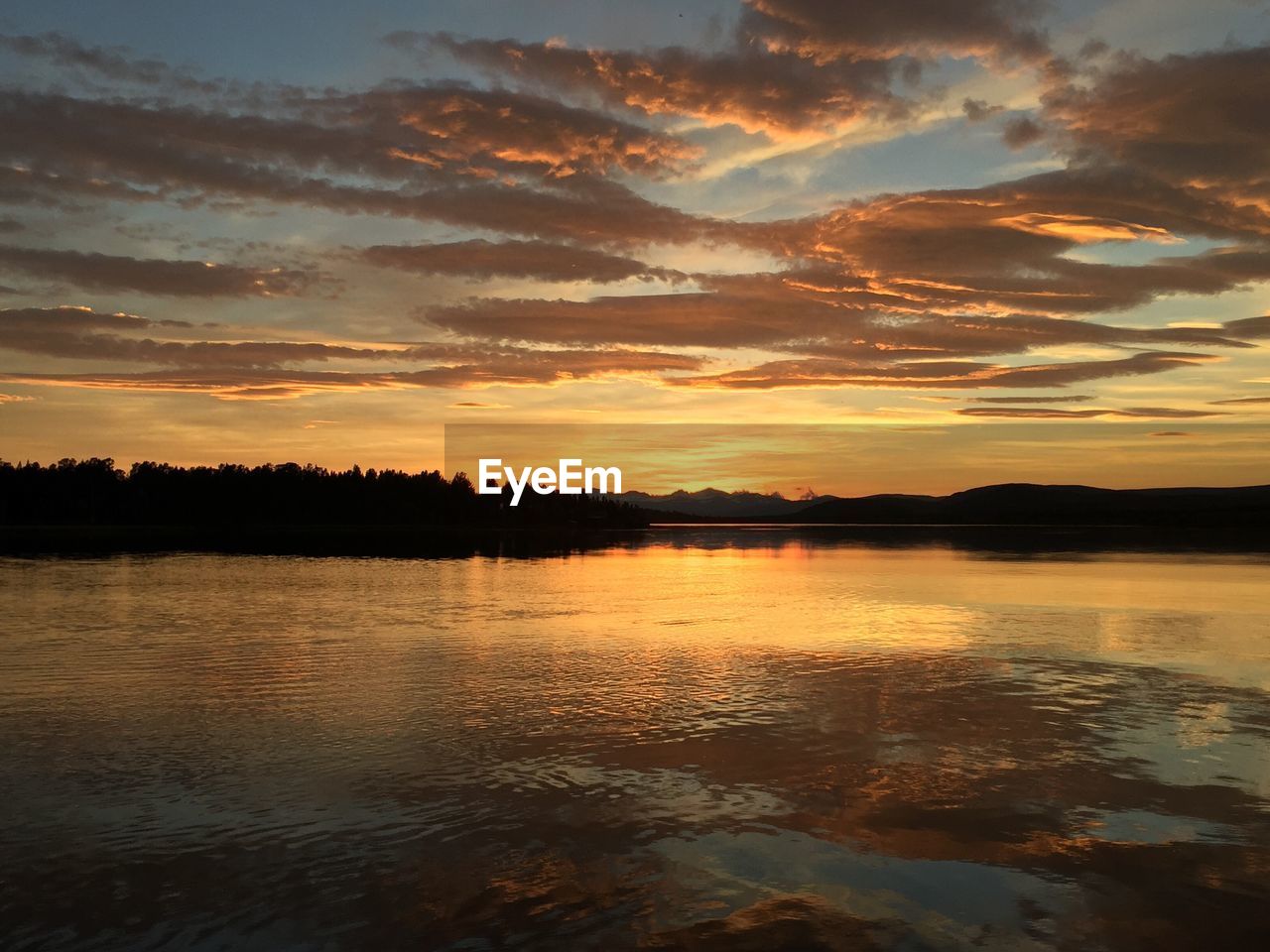 Scenic view of river with silhouetted trees against cloudy sky at dusk