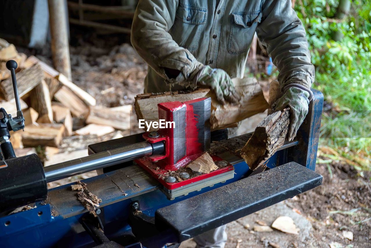 Hydraulic log splitter blade cuts into wood with workman and woodpile