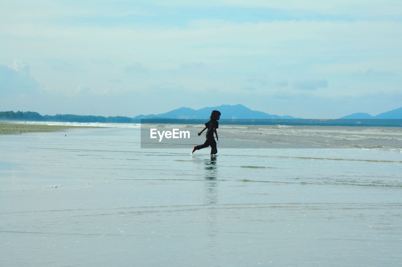 Side view of girl running at beach against sky