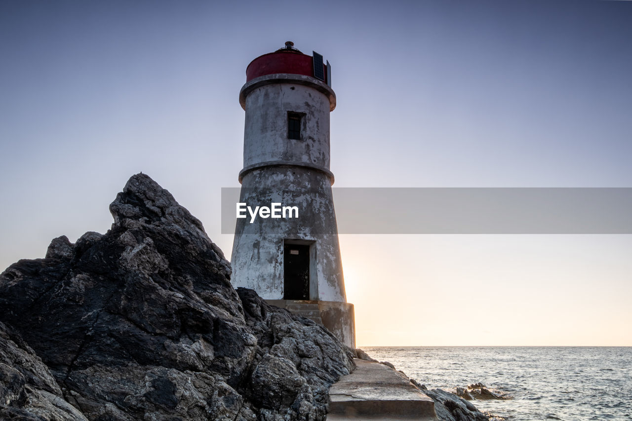Lighthouse by sea against clear sky