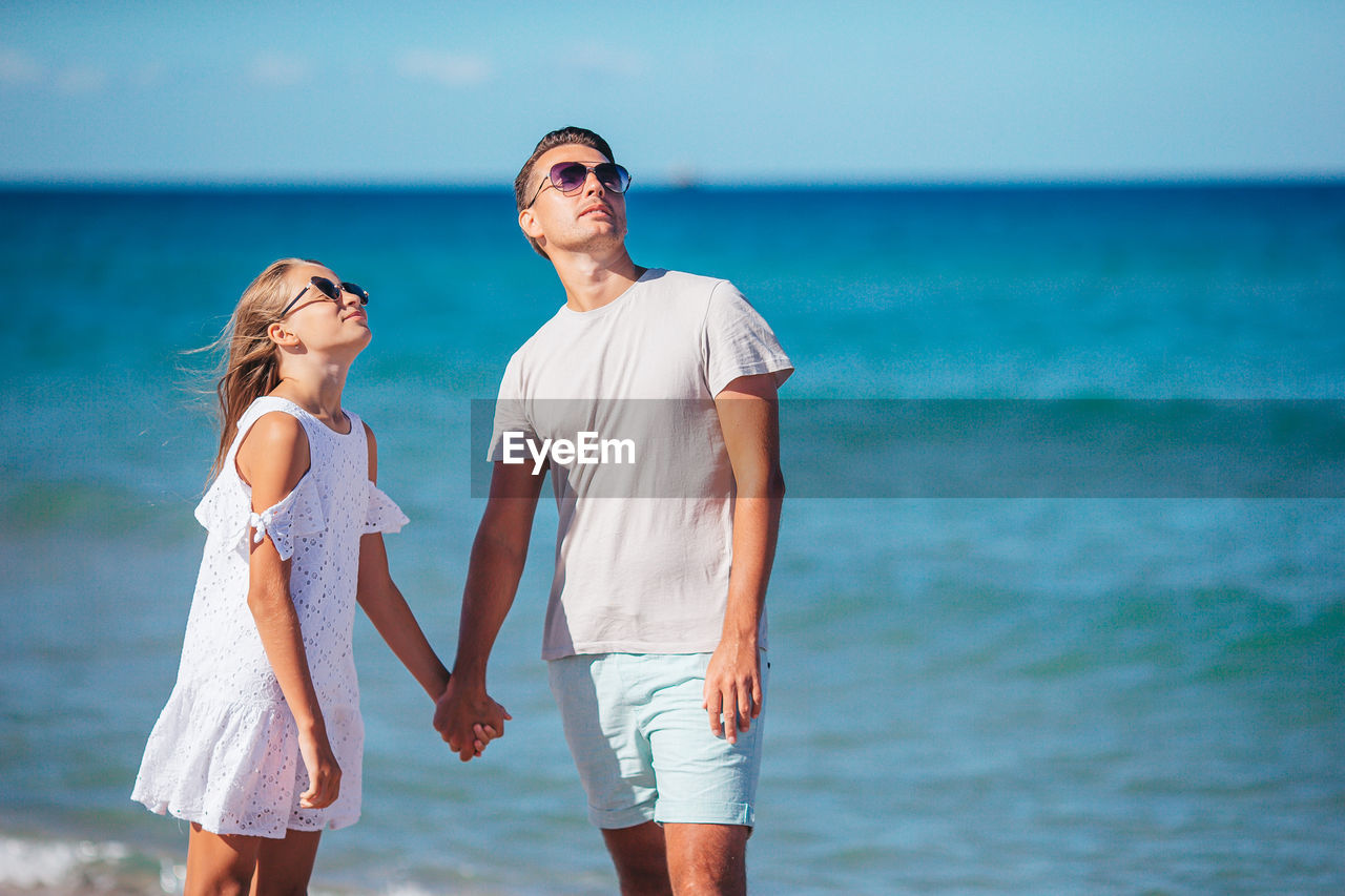 portrait of smiling friends standing at beach against sky