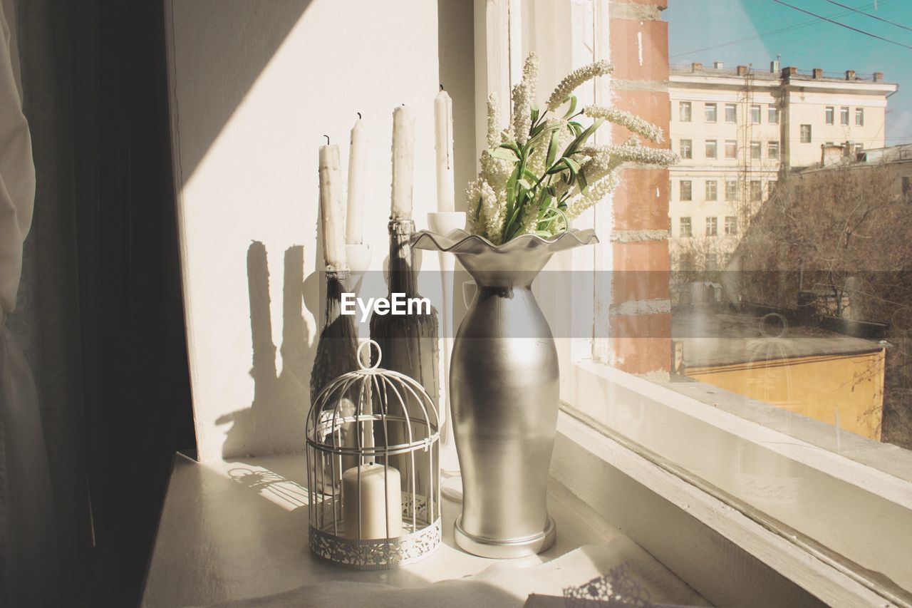 Close-up of decorative candles beside silver vase on windowsill