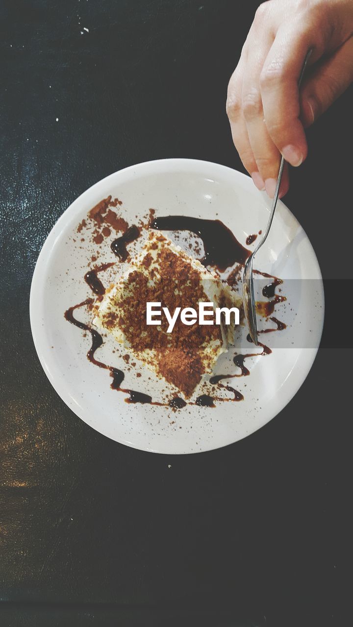 Cropped hand of person slicing tiramisu in spoon