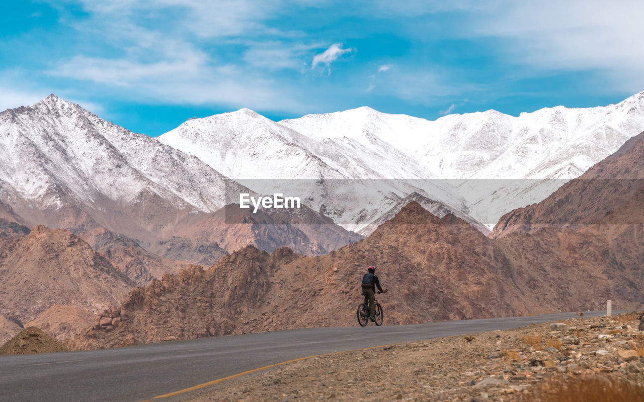 Rear view of man riding bicycle by mountains