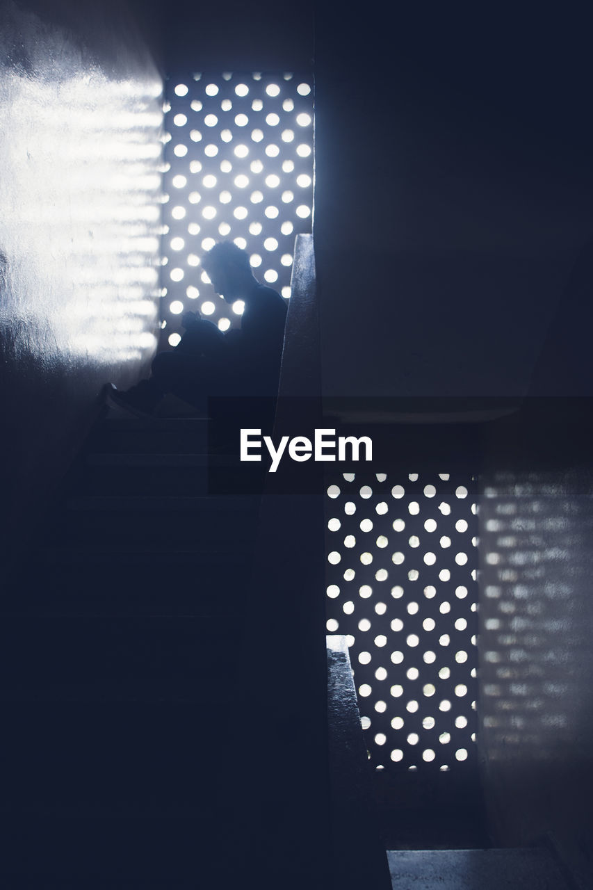 Silhouette of man sitting on staircase in building