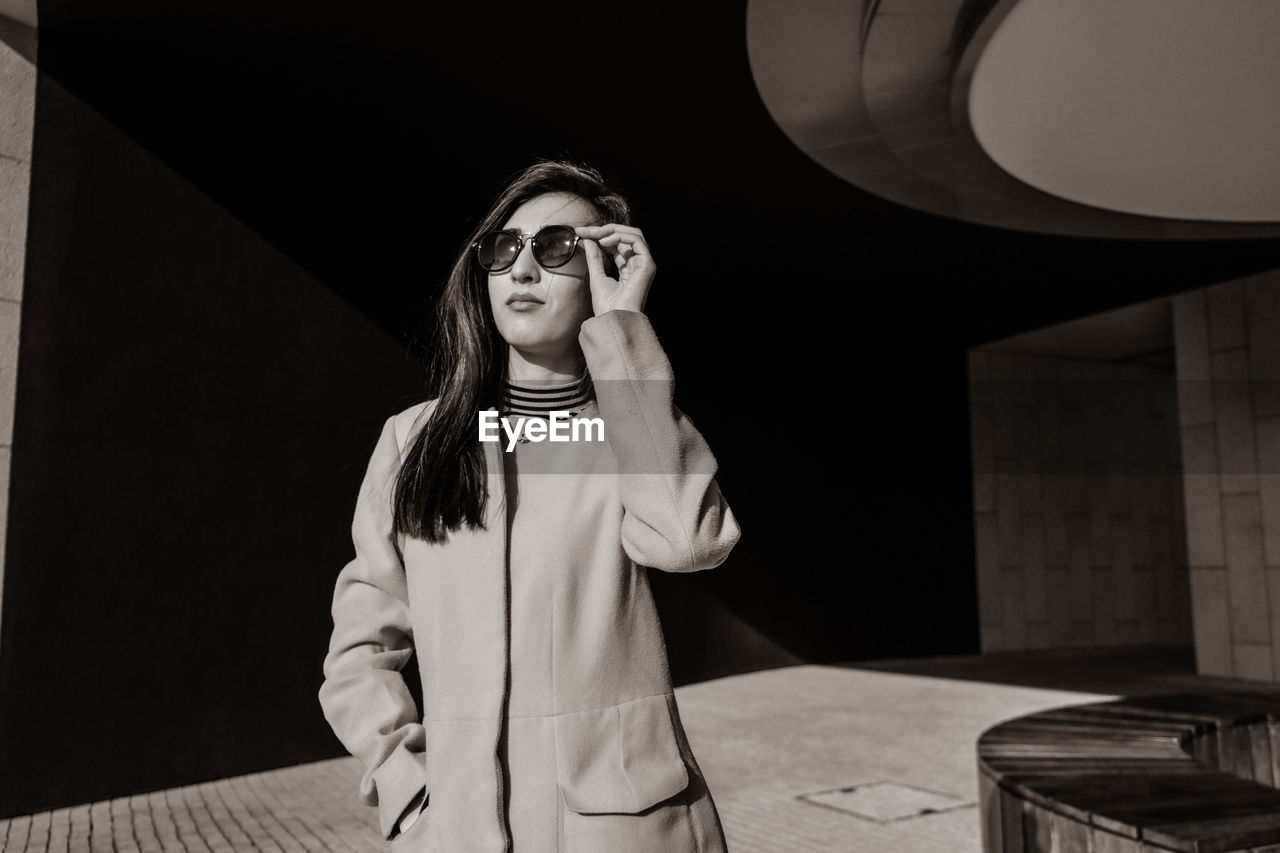 Fashionable woman wearing sunglasses while standing on footpath during sunny day