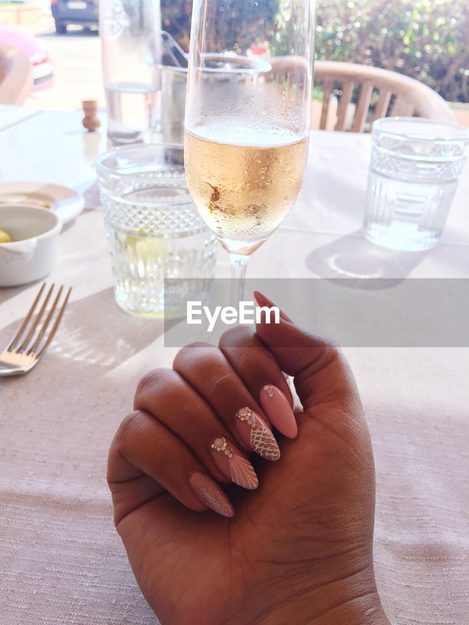 Cropped hand of woman showing nail art by drink on table