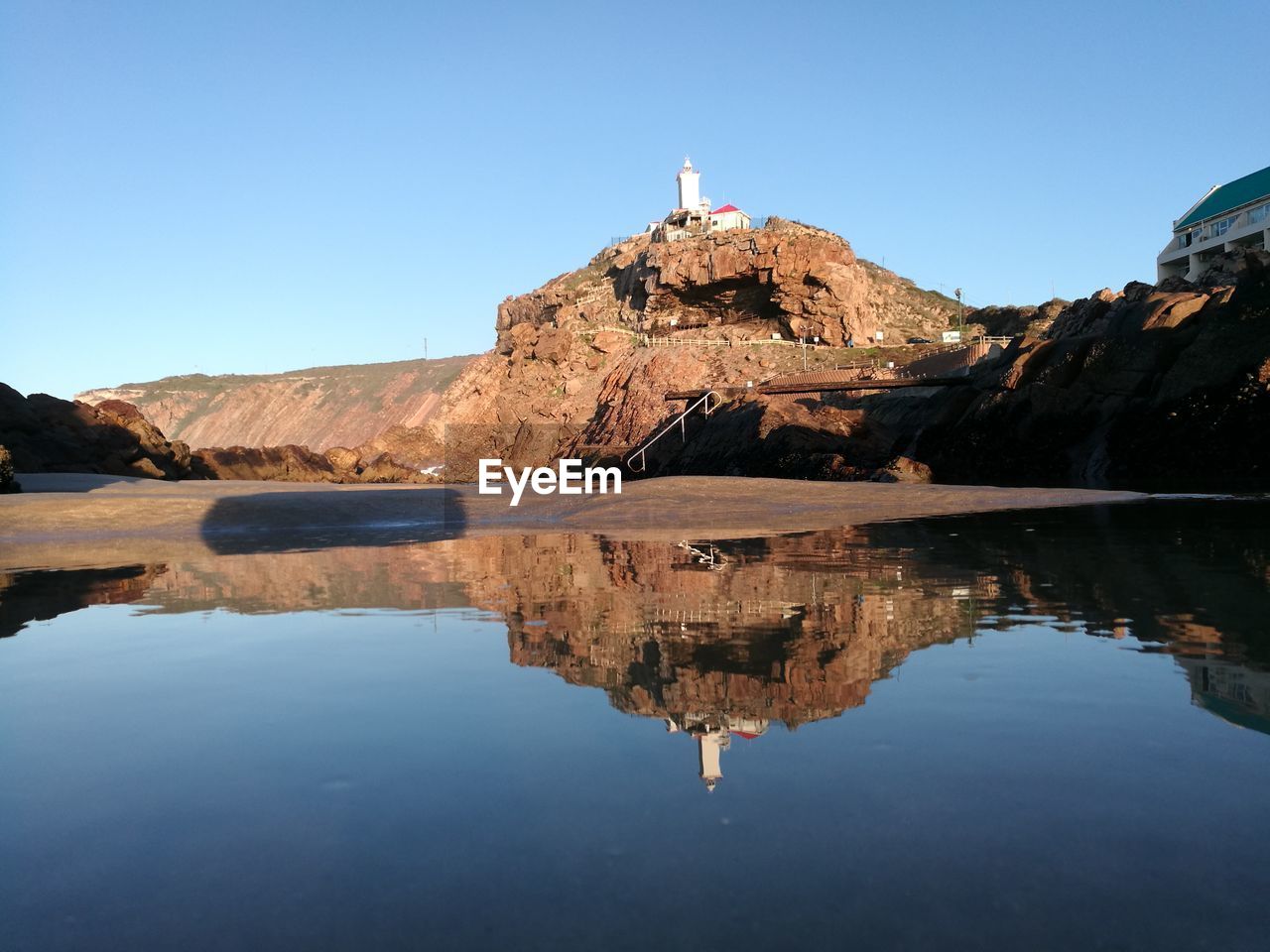 REFLECTION OF LIGHTHOUSE ON WATER AGAINST ROCK