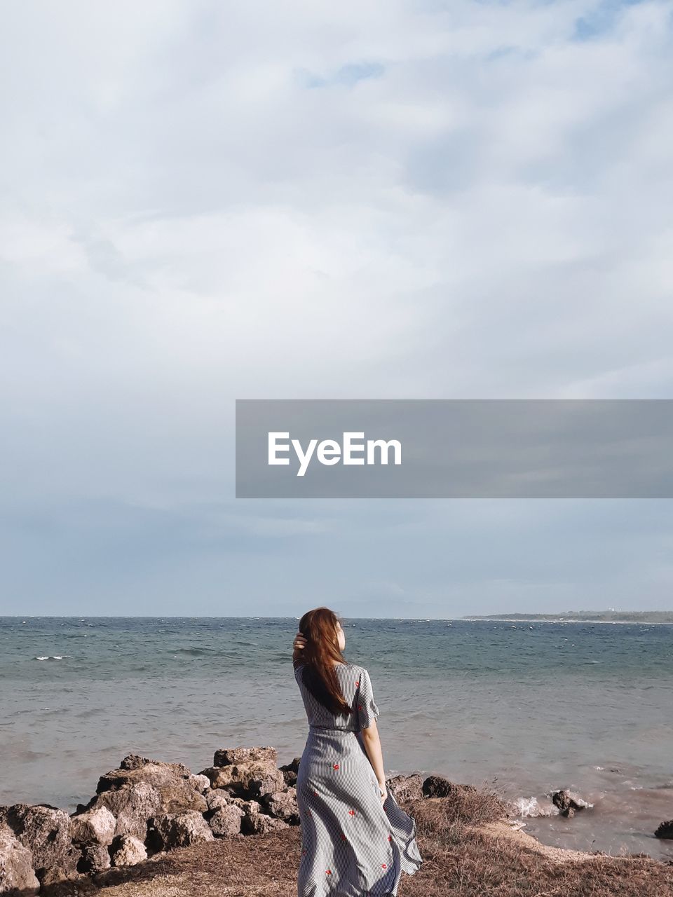 Rear view of woman standing on shore at beach against sky