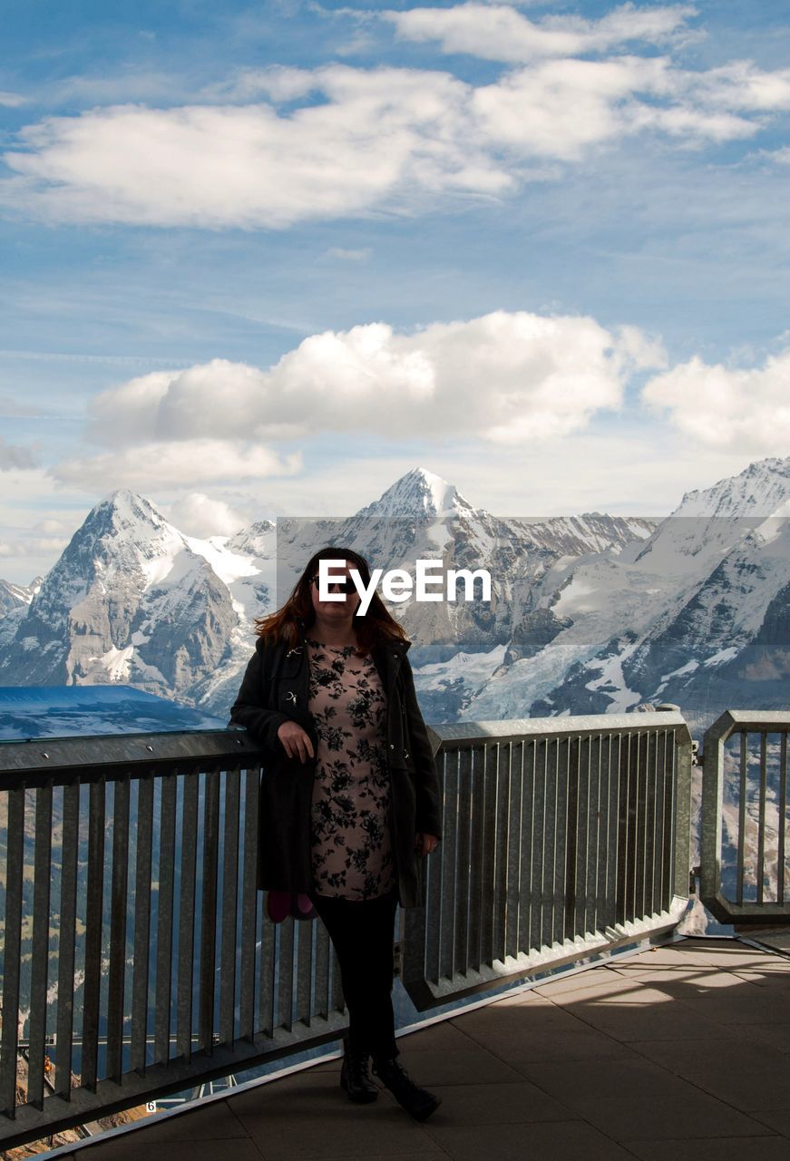 Portrait of woman standing with snowcapped mountain in background against cloudy sky