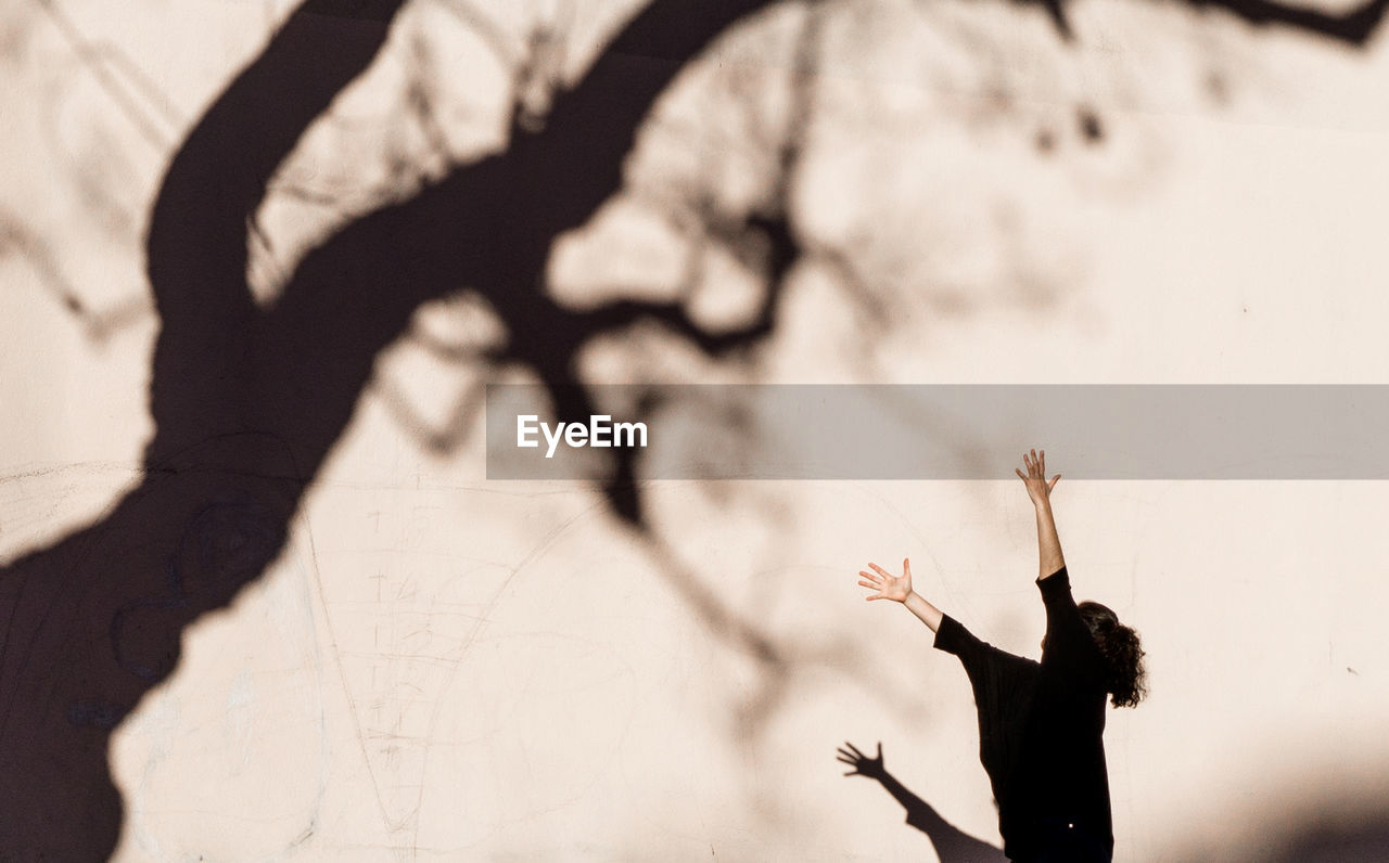 Side view of woman gesturing towards tree shadow on wall