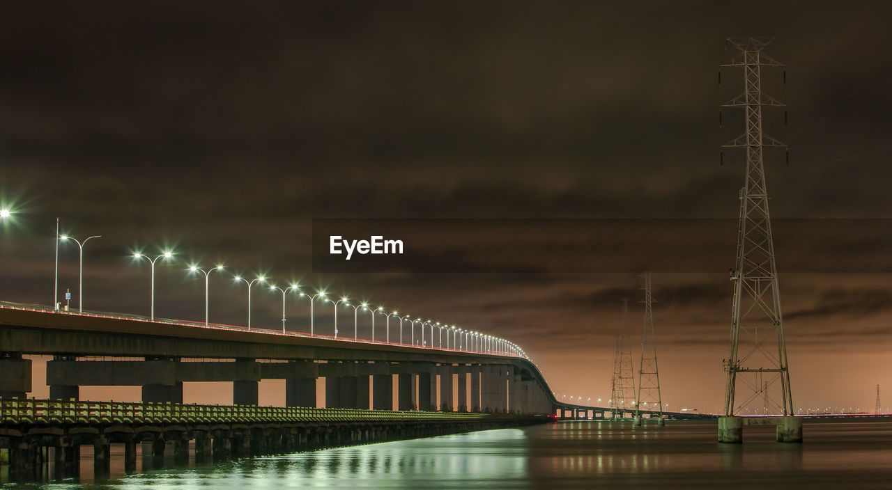 Illuminated san mateo-hayward bridge over river against cloudy sky at night