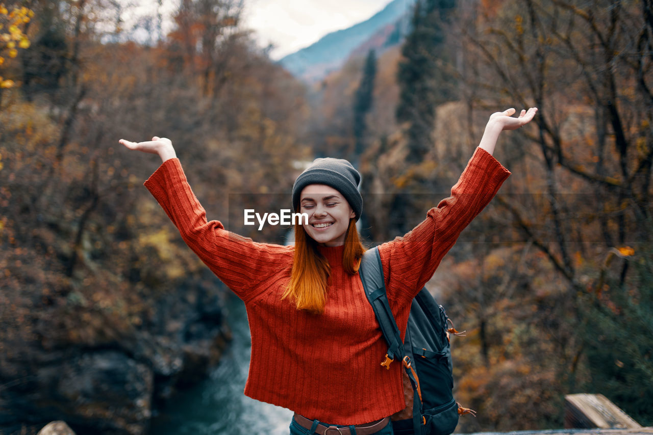 SMILING YOUNG WOMAN WITH ARMS OUTSTRETCHED STANDING IN AUTUMN