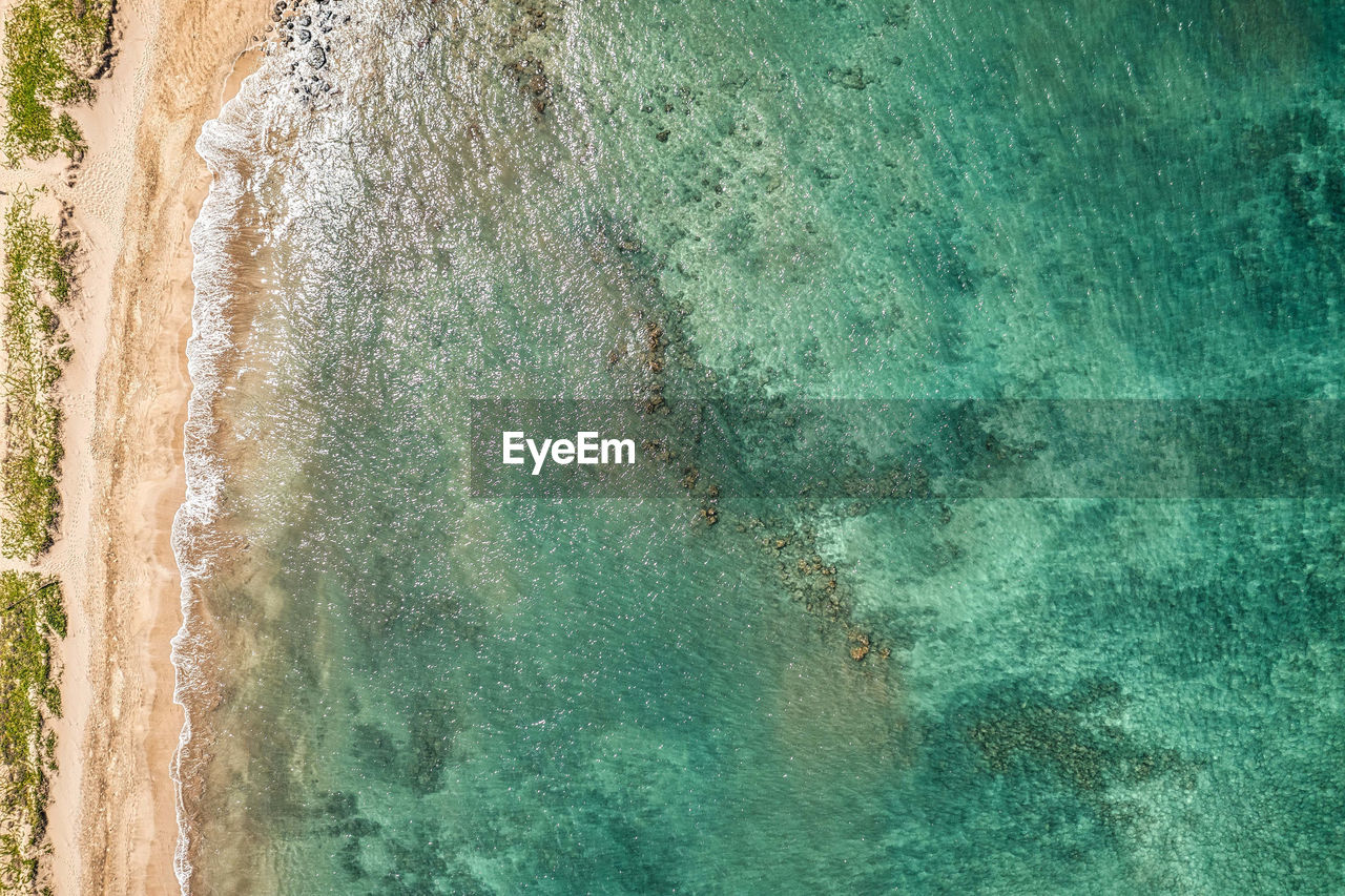 Top down view into teal water from beautiful hawaiian island of maui with white sand beach