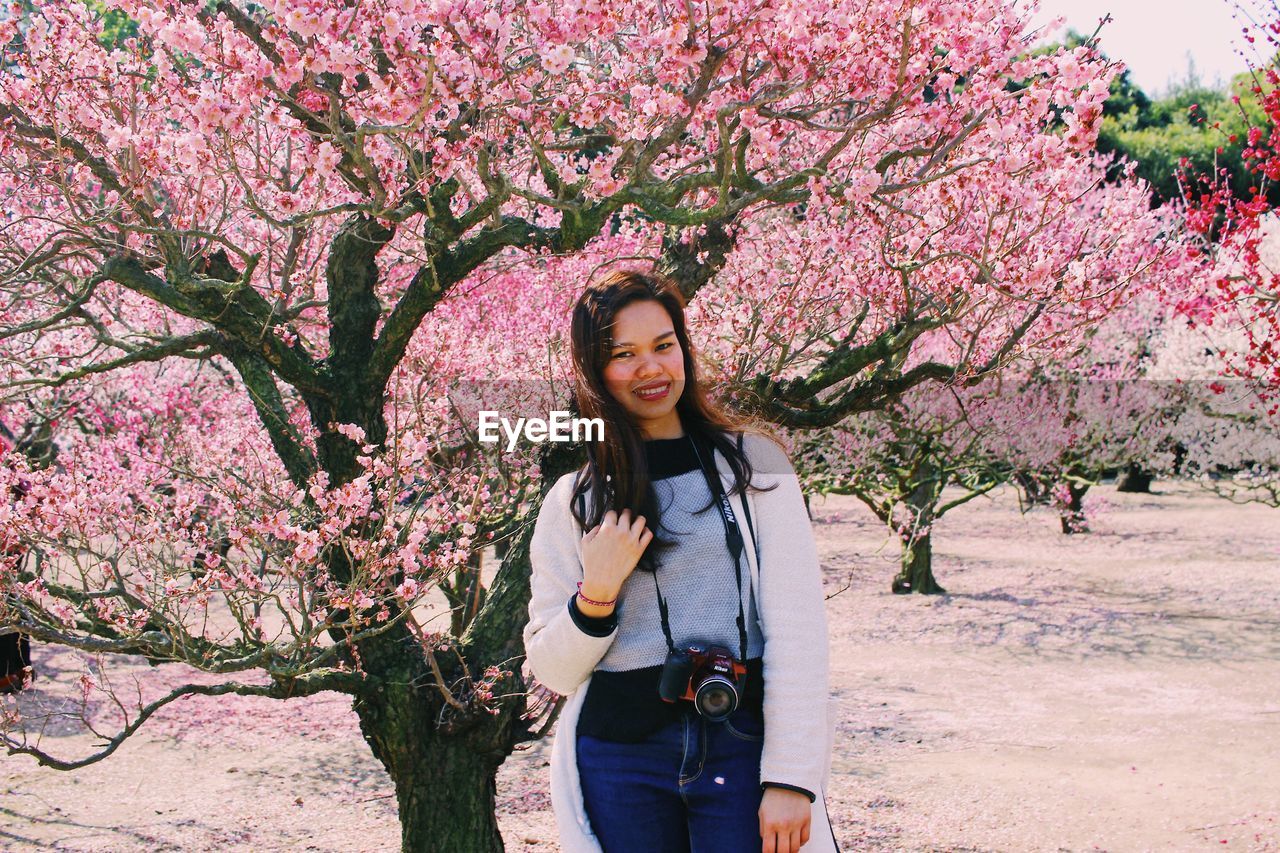 PORTRAIT OF YOUNG WOMAN STANDING BY CHERRY TREE