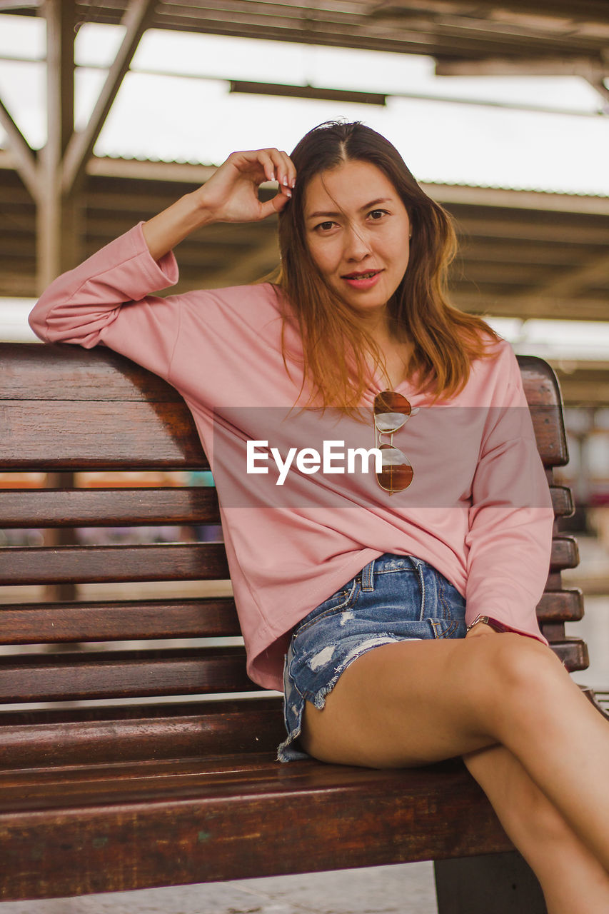 Portrait of woman sitting on bench at railroad station platform