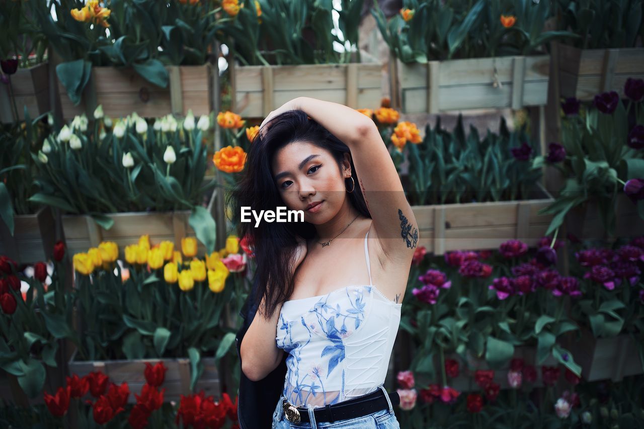 PORTRAIT OF BEAUTIFUL YOUNG WOMAN STANDING BY FLOWER PLANTS