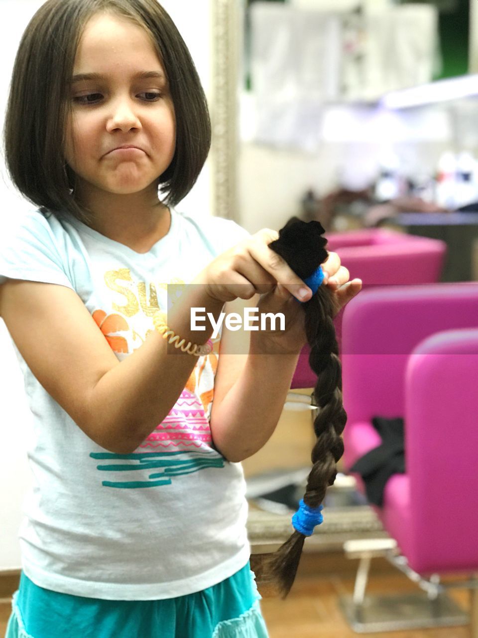 Girl holding pony tail while standing at hair salon 